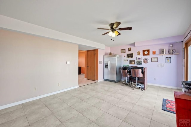 interior space with ceiling fan, light tile patterned floors, baseboards, and stainless steel fridge with ice dispenser