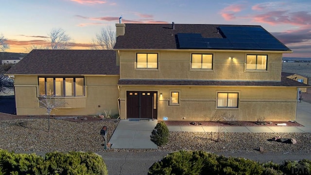 view of front facade featuring solar panels, roof with shingles, and stucco siding