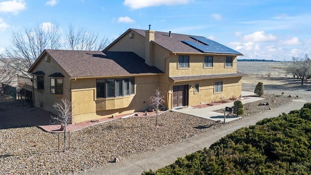 rear view of property with solar panels, roof with shingles, a patio, and stucco siding