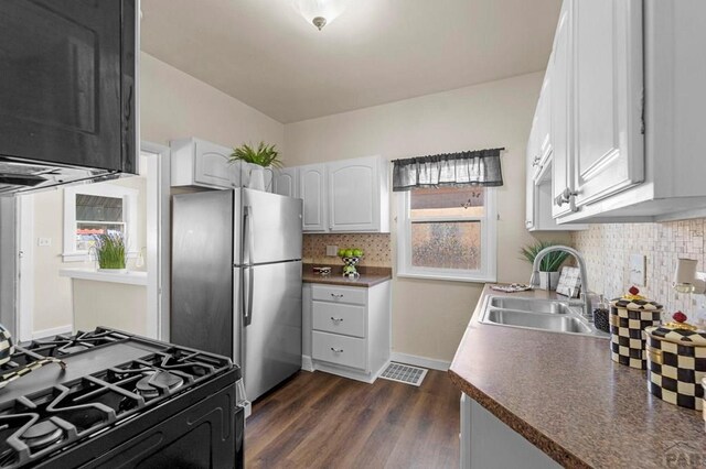 kitchen featuring black range with gas cooktop, visible vents, freestanding refrigerator, white cabinetry, and a sink