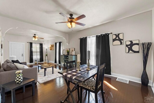 dining room with arched walkways, dark wood-style flooring, visible vents, and baseboards