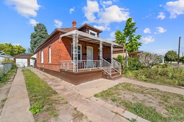 view of front of property with a porch, brick siding, a detached garage, fence, and a chimney