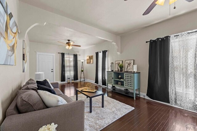 living area featuring ceiling fan, baseboards, dark wood finished floors, and arched walkways