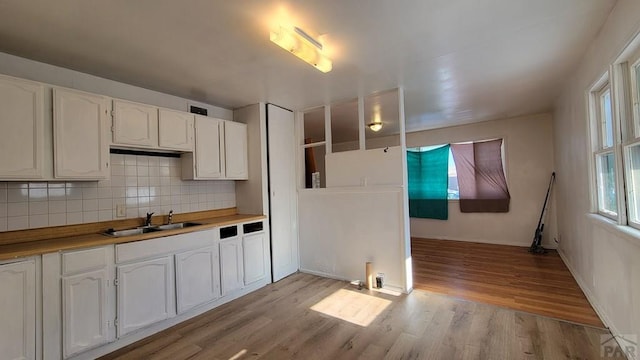 kitchen featuring light wood-style flooring, butcher block countertops, a sink, white cabinetry, and backsplash