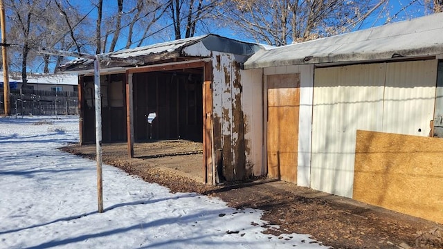 snow covered structure featuring an outbuilding and fence