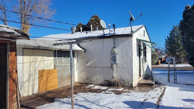 view of snow covered exterior featuring fence and stucco siding