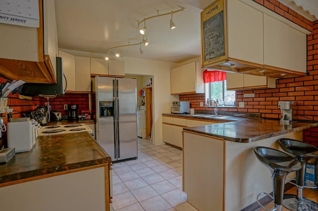 kitchen featuring a sink, a peninsula, dark countertops, and stainless steel fridge