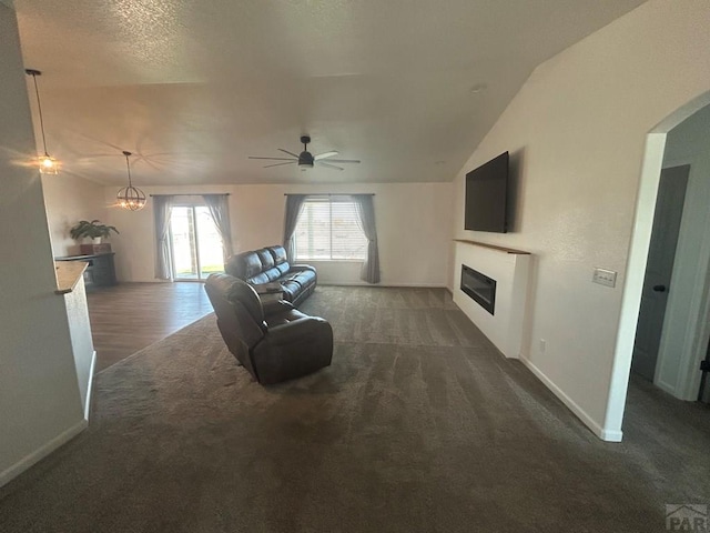 living room featuring ceiling fan, a glass covered fireplace, lofted ceiling, and dark colored carpet