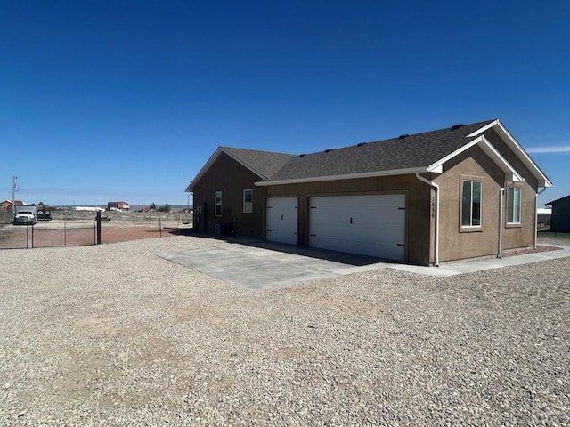 view of home's exterior with fence, roof with shingles, a garage, stucco siding, and driveway
