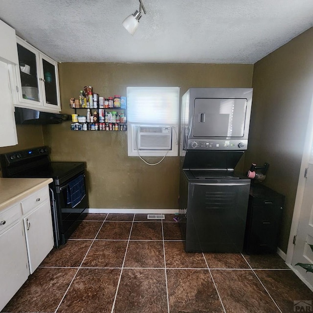 kitchen featuring glass insert cabinets, under cabinet range hood, stacked washing maching and dryer, black range with electric cooktop, and white cabinetry