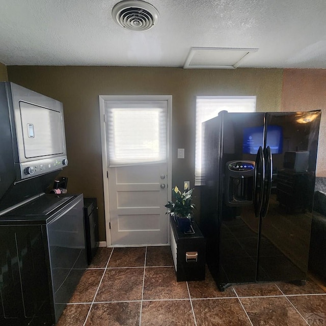 interior space with dark tile patterned flooring, visible vents, a textured ceiling, and stacked washing maching and dryer