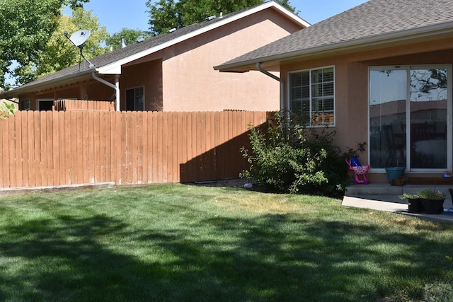 view of property exterior featuring a yard, a shingled roof, fence, and stucco siding