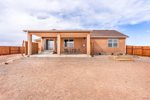 rear view of property featuring a vegetable garden, a patio area, fence, and stucco siding