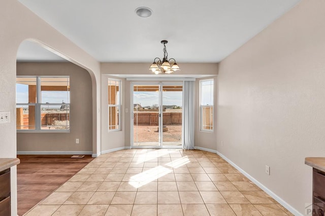 unfurnished dining area featuring baseboards, light tile patterned floors, arched walkways, and an inviting chandelier