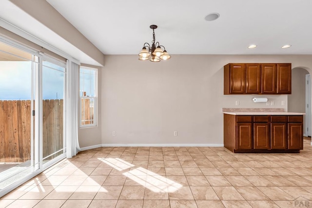 unfurnished dining area with arched walkways, light tile patterned floors, a chandelier, and baseboards