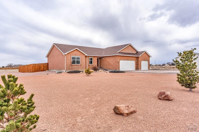 ranch-style home featuring fence, driveway, an attached garage, and stucco siding