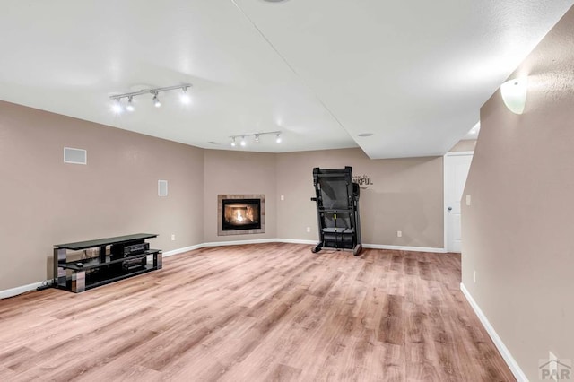 unfurnished living room featuring a glass covered fireplace, rail lighting, light wood-style flooring, and baseboards