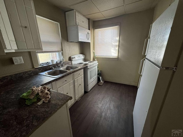 kitchen featuring white appliances, white cabinets, a drop ceiling, dark countertops, and a sink