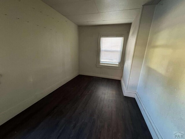 unfurnished room featuring a drop ceiling, dark wood finished floors, and baseboards