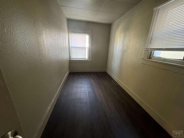 empty room with visible vents, dark wood-type flooring, a paneled ceiling, and baseboards