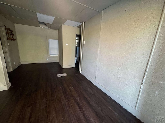 spare room with baseboards, a drop ceiling, and dark wood-type flooring