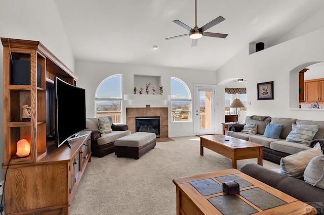 living area with high vaulted ceiling, a tile fireplace, light carpet, and ceiling fan