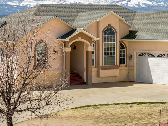 view of front of property featuring a mountain view, a garage, driveway, roof with shingles, and stucco siding