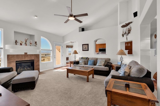 living room featuring light colored carpet, a tiled fireplace, a ceiling fan, high vaulted ceiling, and baseboards