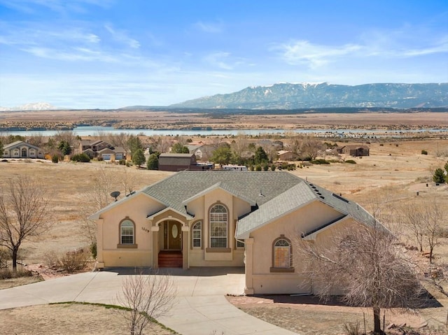 view of front of property featuring a shingled roof, a water and mountain view, and stucco siding