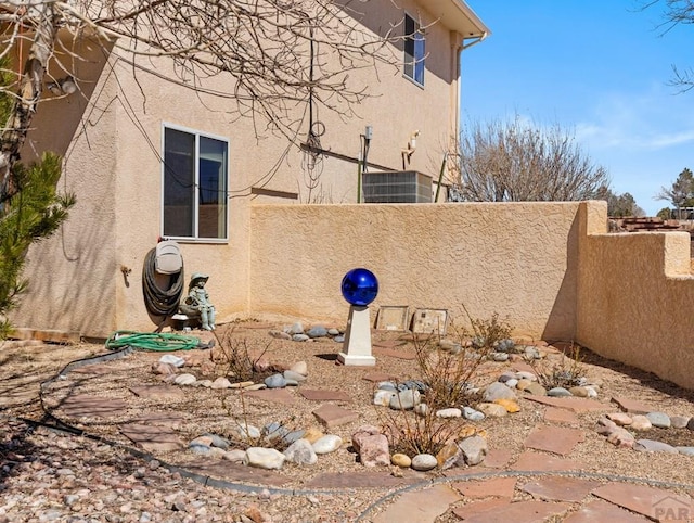 view of side of home featuring cooling unit, fence, and stucco siding