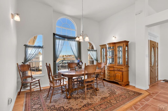 dining space featuring light wood-style floors, a high ceiling, baseboards, and a notable chandelier