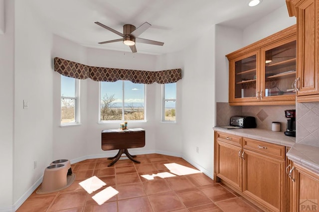 kitchen with glass insert cabinets, backsplash, tile countertops, and a ceiling fan