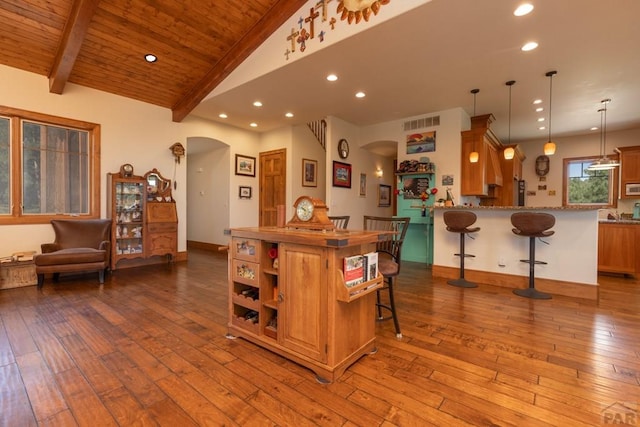 kitchen with arched walkways, brown cabinets, vaulted ceiling with beams, wood-type flooring, and a kitchen breakfast bar