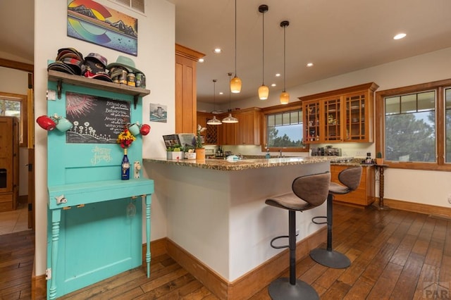 kitchen featuring brown cabinetry, stone countertops, glass insert cabinets, and dark wood finished floors