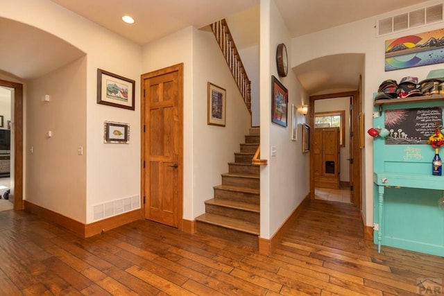 foyer entrance featuring arched walkways, visible vents, hardwood / wood-style floors, baseboards, and stairs