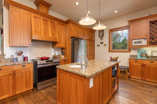 kitchen with light stone counters, a center island with sink, stainless steel appliances, a sink, and hardwood / wood-style flooring