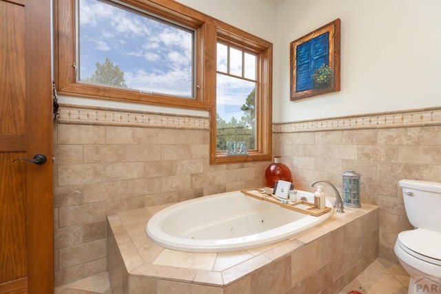 bathroom featuring tile patterned flooring, toilet, tile walls, a jetted tub, and wainscoting