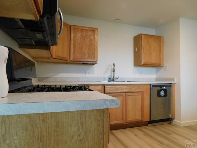 kitchen with light countertops, light wood-style flooring, appliances with stainless steel finishes, a sink, and baseboards