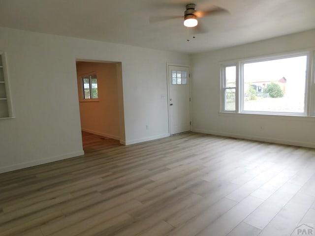 unfurnished room with light wood-type flooring, a ceiling fan, and baseboards