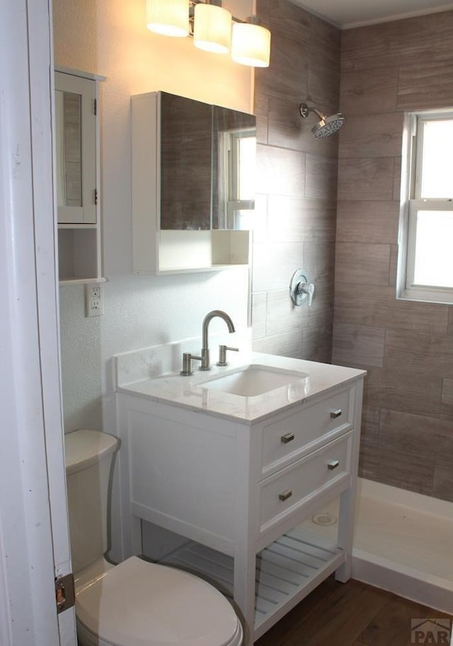 bathroom featuring vanity, tiled shower, wood finished floors, and toilet