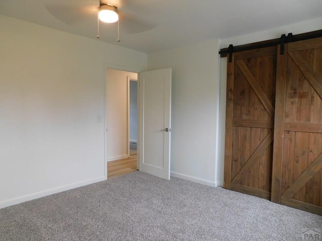 unfurnished bedroom with a barn door, carpet flooring, a ceiling fan, and baseboards