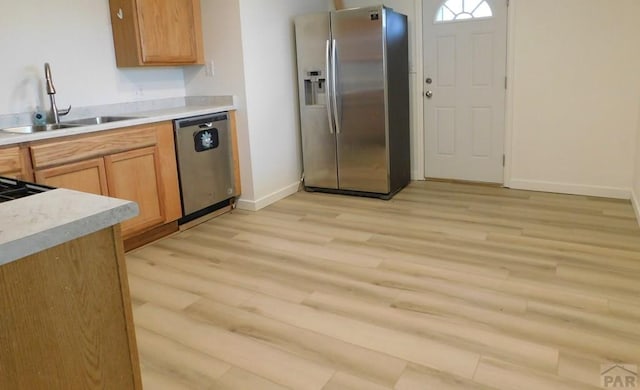 kitchen featuring light wood-style flooring, stainless steel appliances, a sink, and light countertops