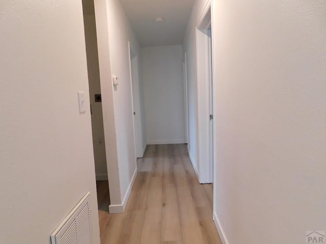 hall with light wood-style flooring, visible vents, and baseboards