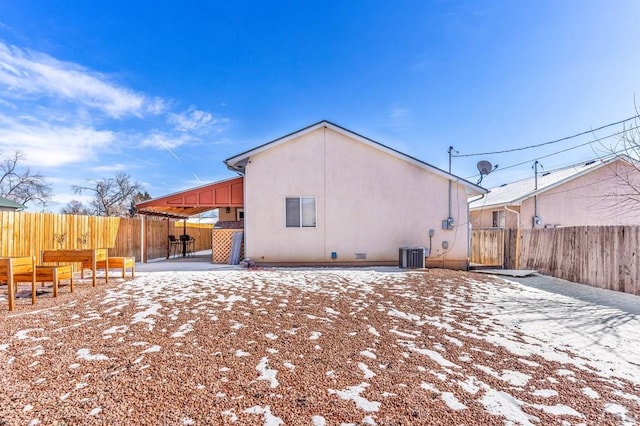 snow covered property featuring a patio area, a fenced backyard, central AC, and stucco siding