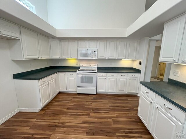 165 Kingsley Ave Unit M, Pueblo, CO 81005 - kitchen featuring white appliances, dark countertops, dark wood-type flooring, white cabinetry, and a towering ceiling