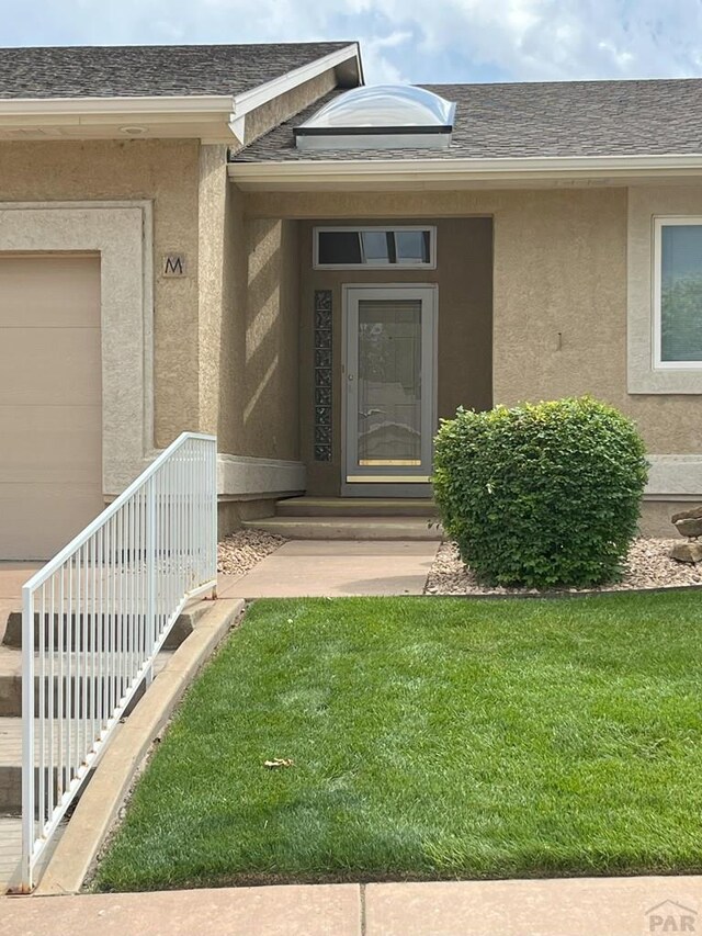 165 Kingsley Ave Unit M, Pueblo, CO 81005 - doorway to property featuring stucco siding, roof with shingles, and a lawn