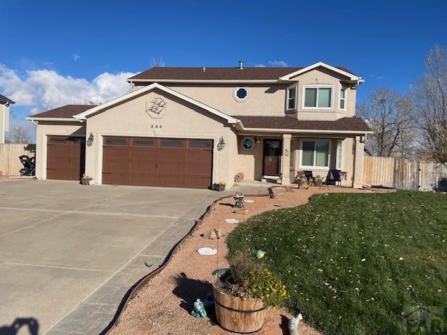 traditional-style home with stucco siding, fence, a garage, driveway, and a front lawn