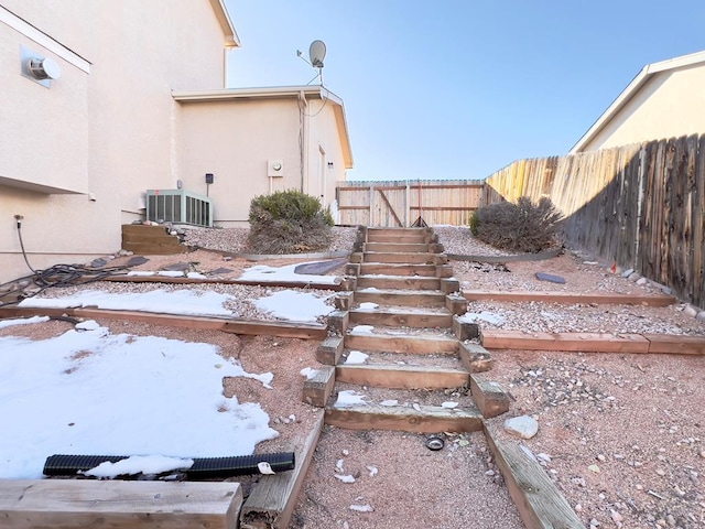 yard covered in snow featuring stairs, central AC unit, and a fenced backyard