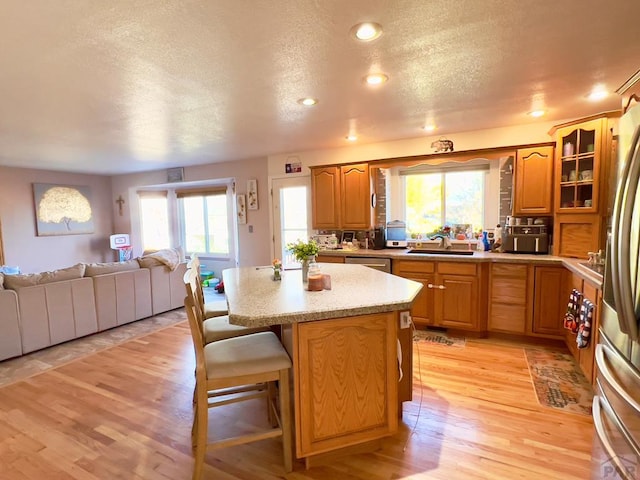 kitchen with a breakfast bar area, light countertops, glass insert cabinets, open floor plan, and a sink