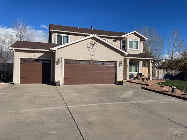 traditional home featuring driveway, an attached garage, fence, and stucco siding